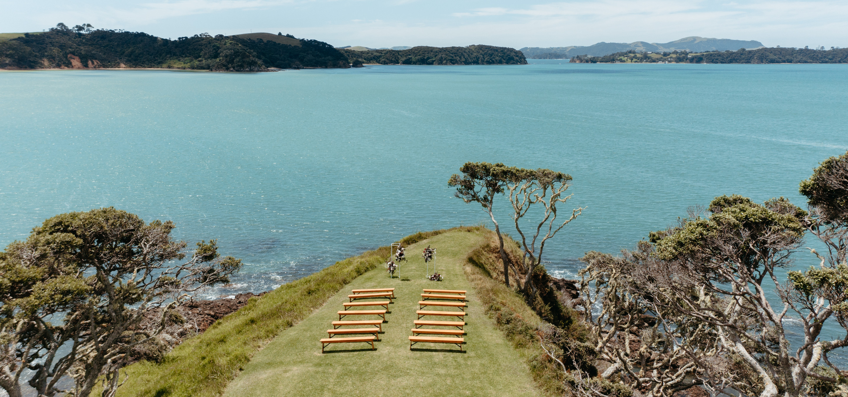 An outdoor wedding ceremony setup with wooden benches on The Point at Baylys' Farm, a stunning coastal venue in the Bay of Islands.