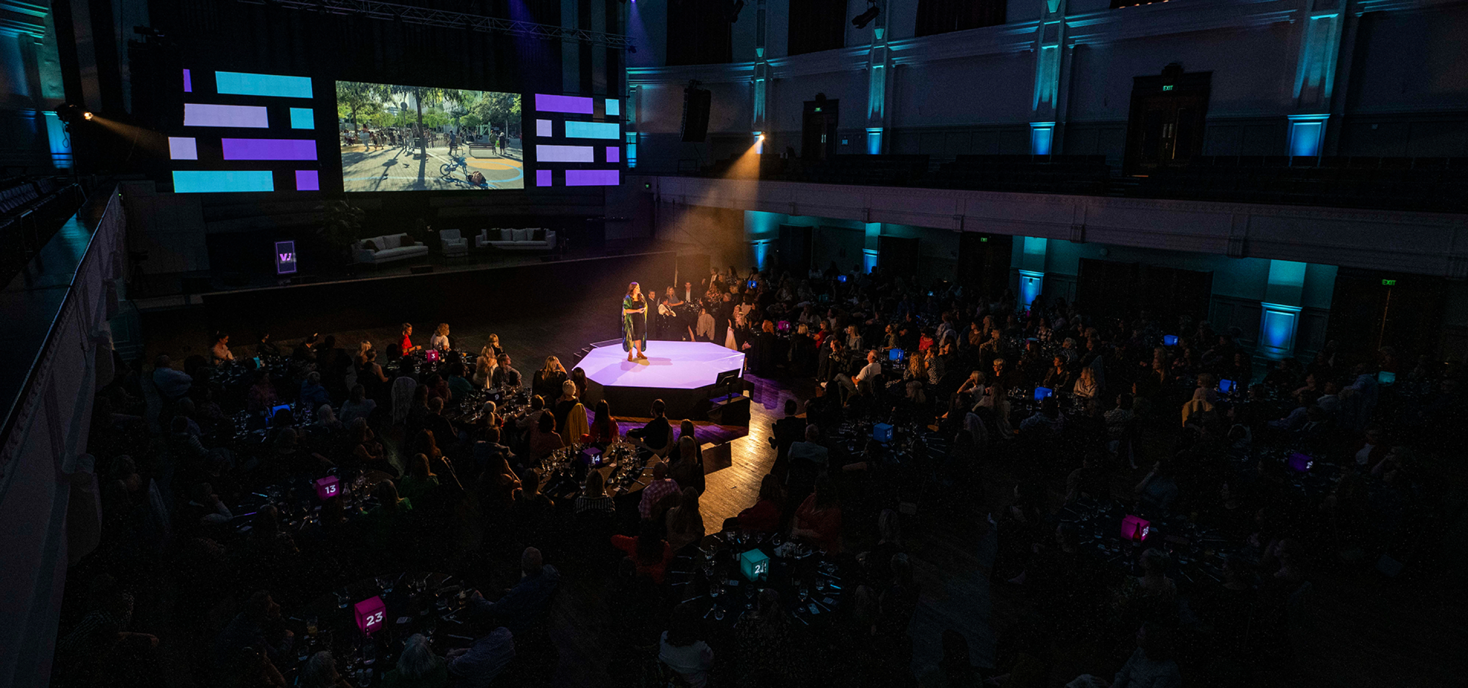 A speaker presents to a large audience in the grand baroque auditorium of The Dunedin Centre, Dunedin.
