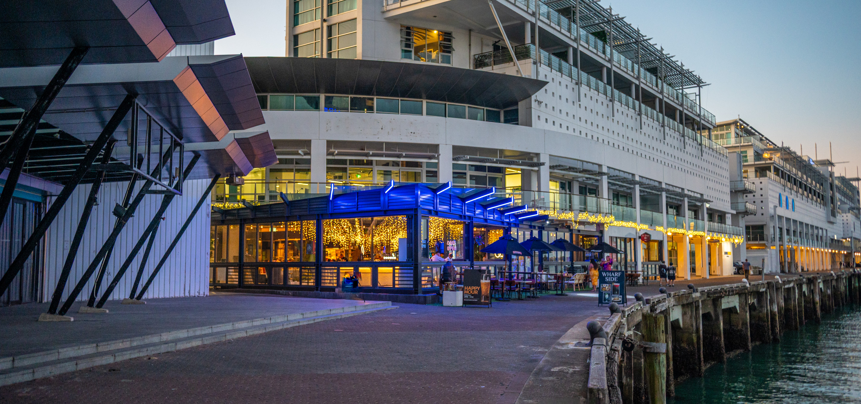 A modern, illuminated outdoor dining and bar area at Wharfside Function Centre, Auckland, overlooking the waterfront.