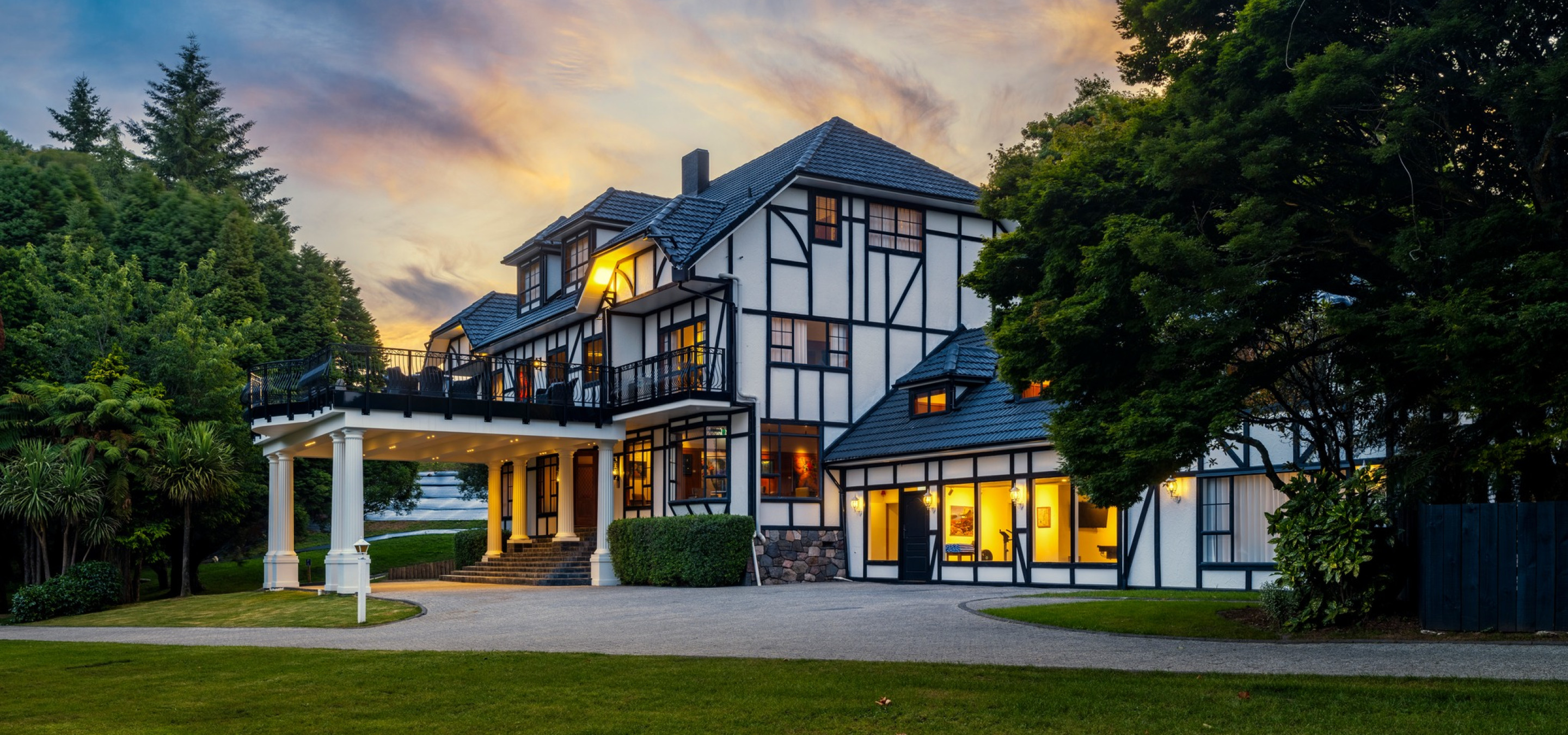 The elegant Tudor-style exterior of Hana Lodge in Rotorua is beautifully illuminated at dusk.