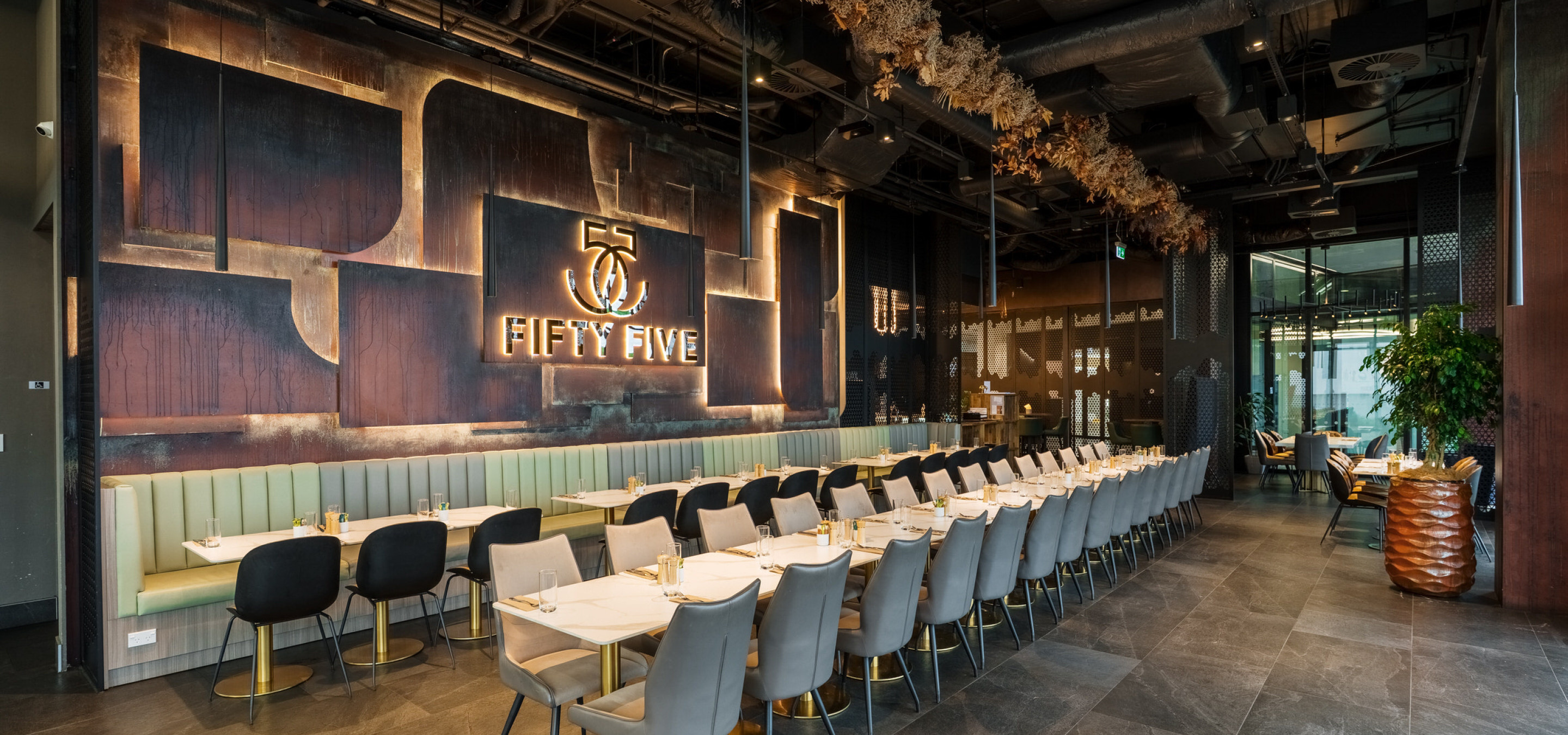 A chic, modern dining area at 55 Cafe in Auckland, featuring long tables, booth seating, and a prominent illuminated 'Fifty Five' sign.