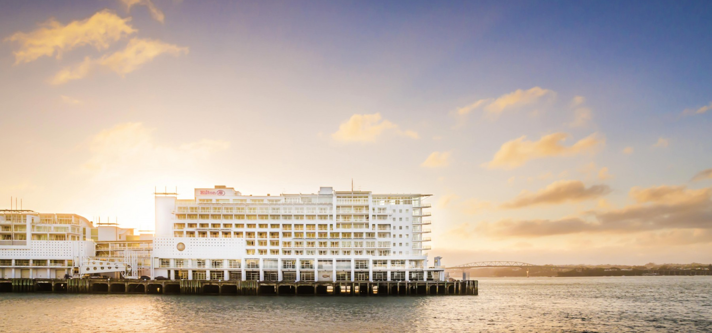 An exterior view of the contemporary, nautical-inspired Hilton Auckland hotel on Princes Wharf at sunset.