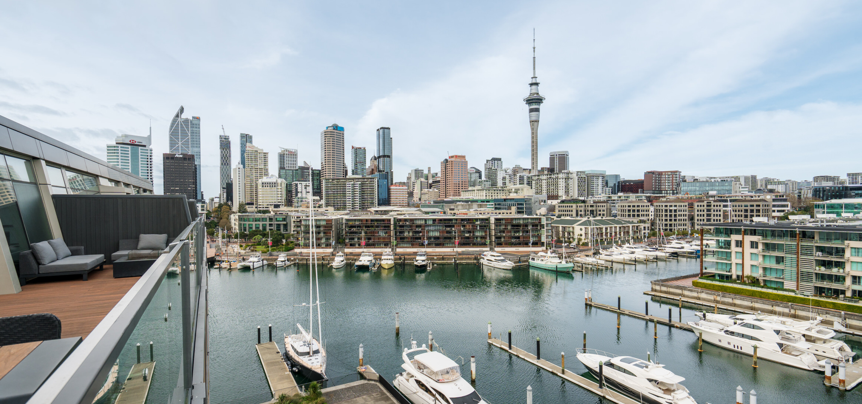 Park Hyatt Auckland's modern waterfront terrace offers lounge seating and panoramic views of the marina and Auckland city skyline.