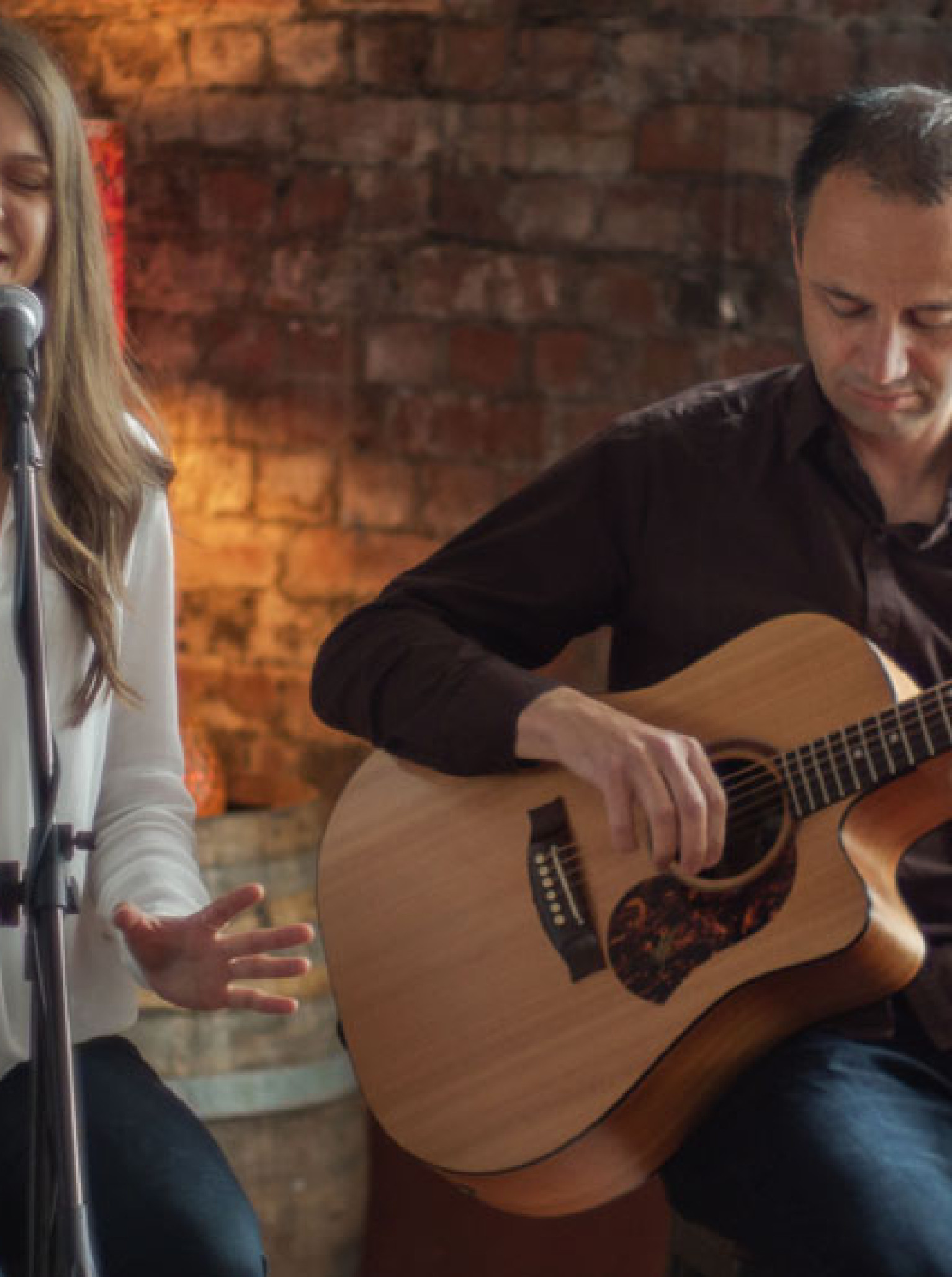 Mish & Wade's acoustic duo performs against a rustic brick wall backdrop at an Auckland venue.
