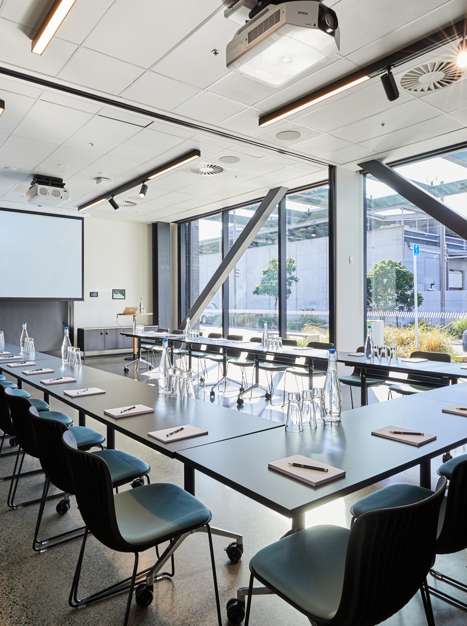 A modern, industrial-chic U-shaped meeting room with a projector screen at 12 Madden St by Precinct Flex in Auckland.