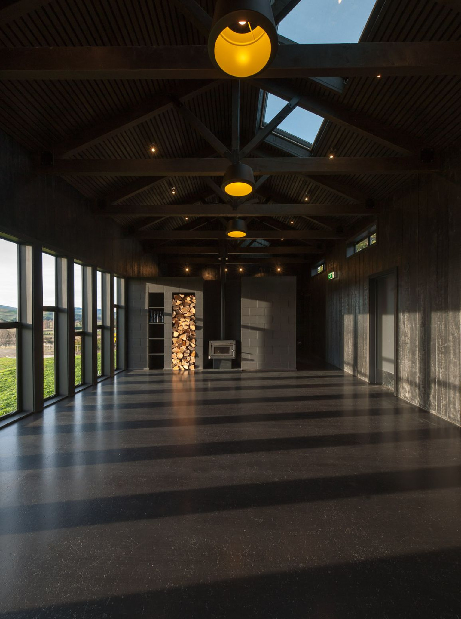 Black Estate Winery, near Christchurch, offers a rural-inspired event space with dark timber, concrete, a fireplace, and vineyard views.