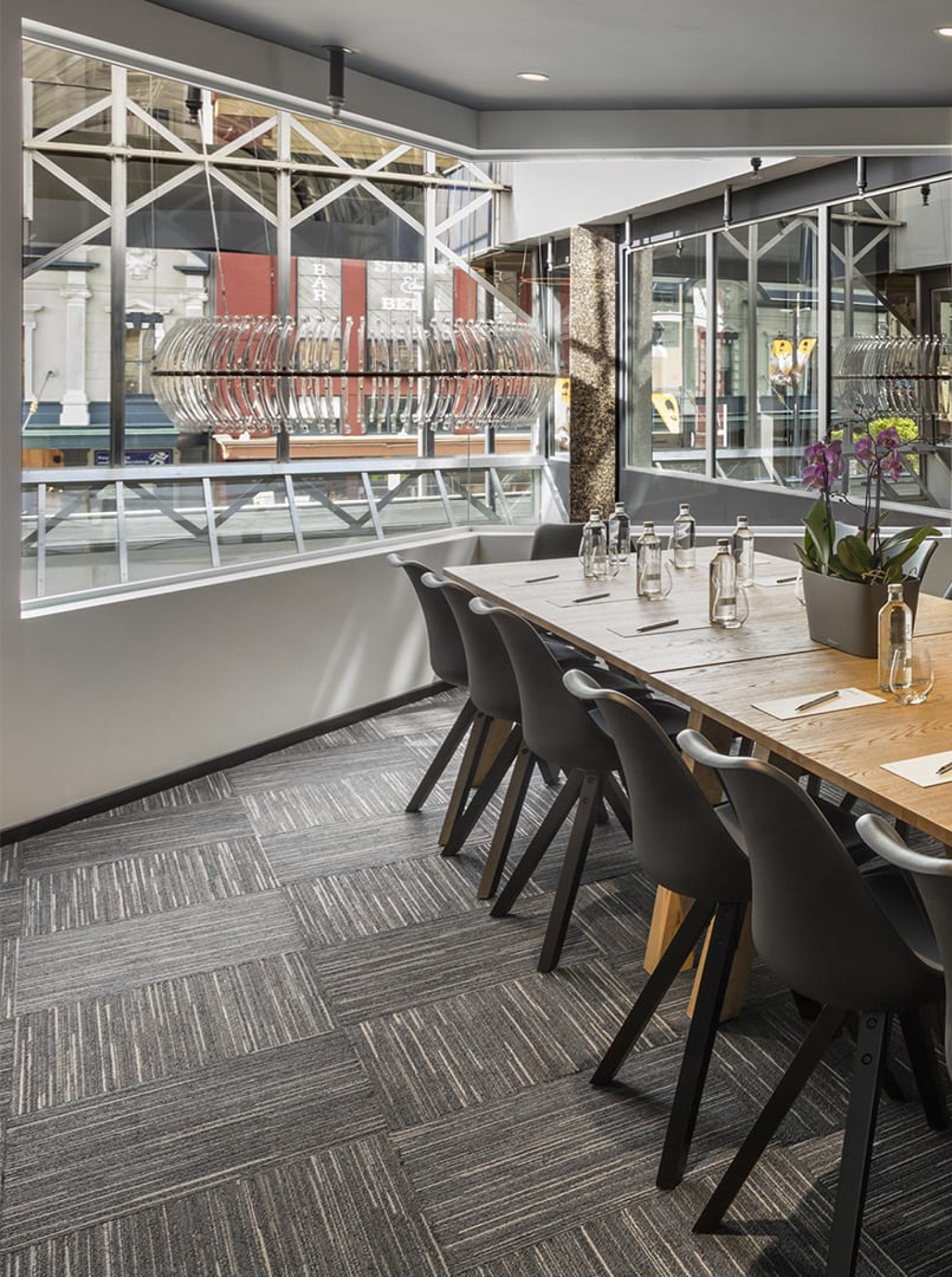 A modern meeting room at the Oaks Wellington Hotel in Wellington, featuring a long wooden table and industrial-chic window details.