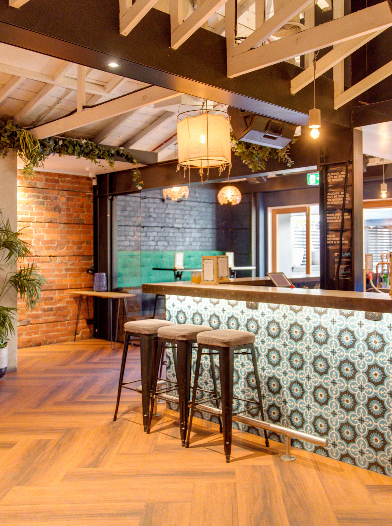 The vibrant bar area at Sassy Loves Cash in Wellington features exposed brick, wooden ceilings, and eclectic patterned tiles.