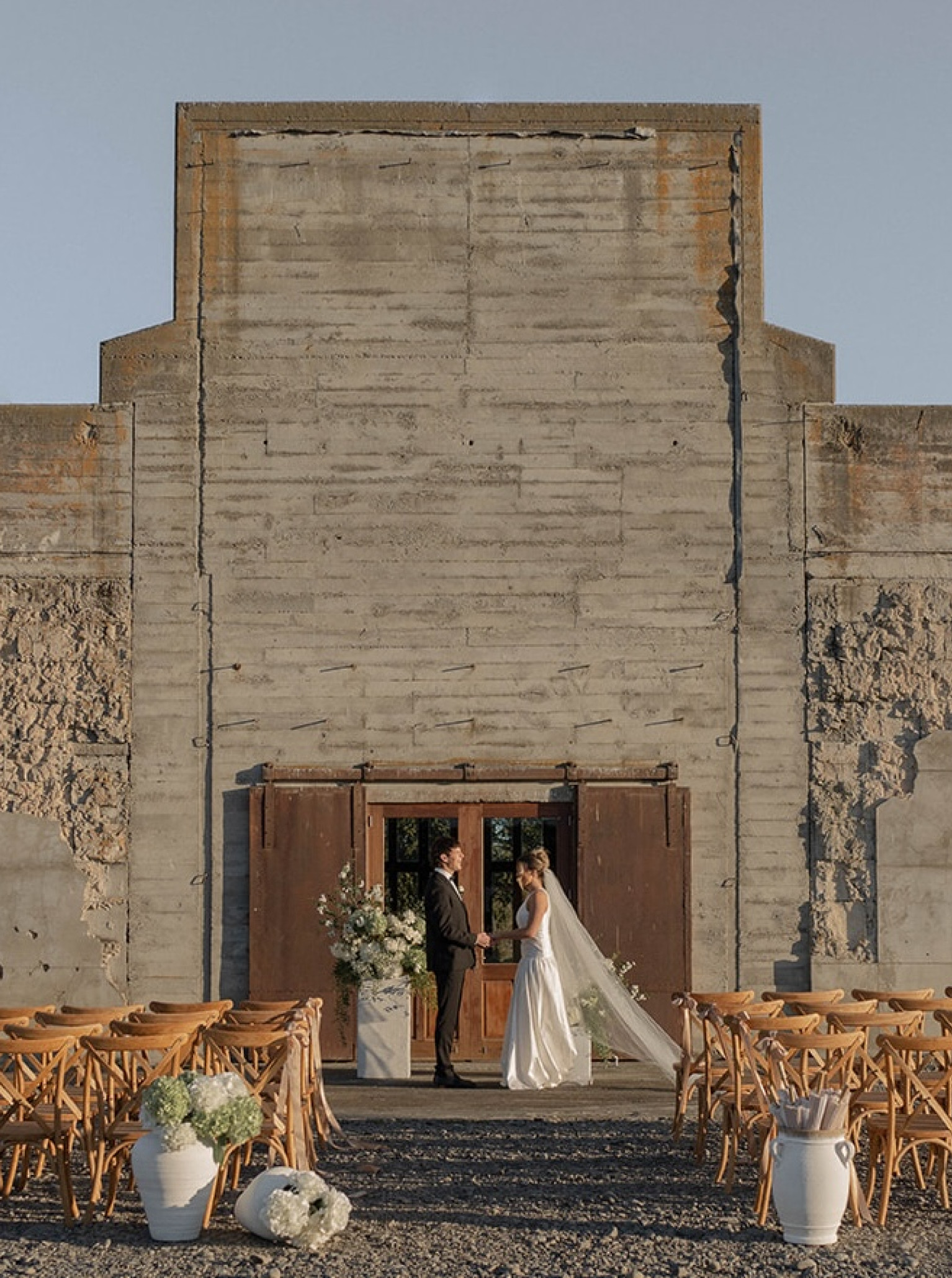 A rustic outdoor wedding ceremony at The Flaxmill, Christchurch, featuring its original industrial concrete walls.