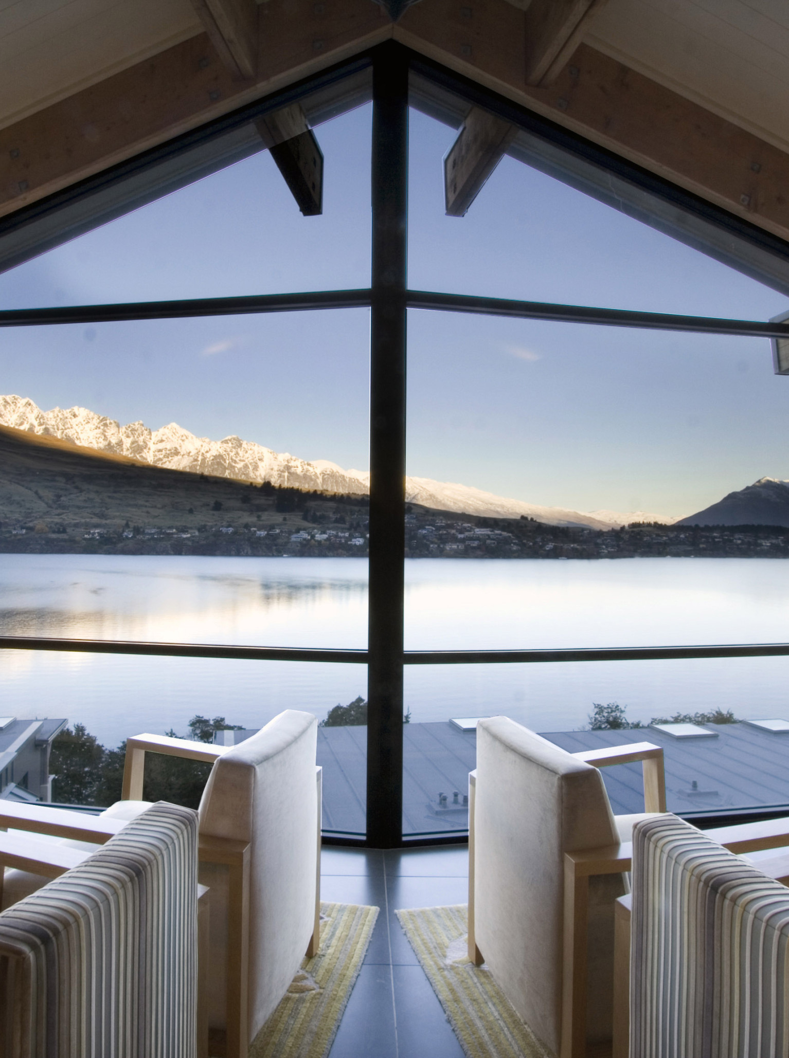 The Rees Hotel, Queenstown, offers a modern lounge with floor-to-ceiling windows framing stunning Lake Wakatipu and mountain views.