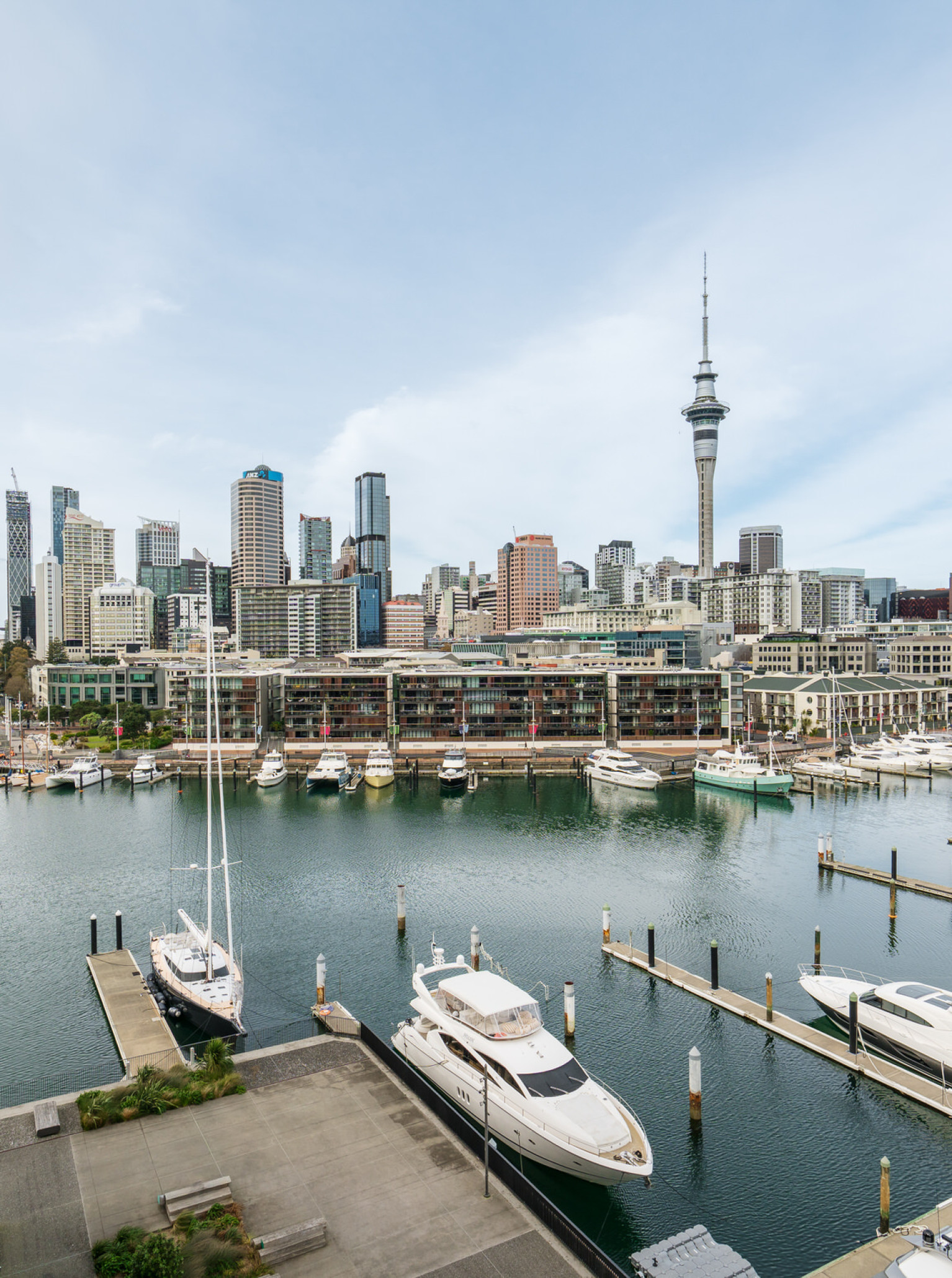 Park Hyatt Auckland's modern waterfront terrace offers lounge seating and panoramic views of the marina and Auckland city skyline.