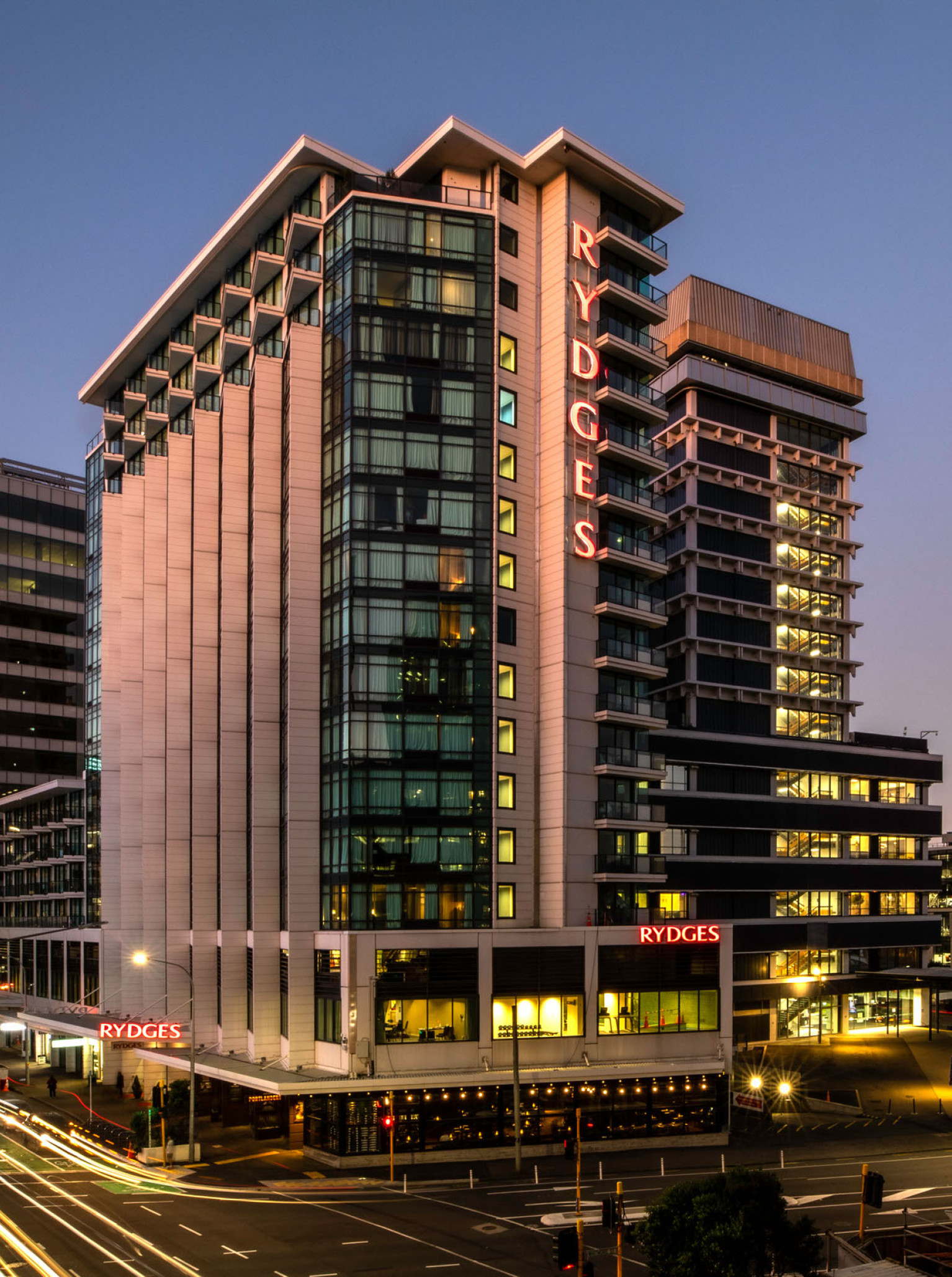 Rydges Wellington's modern slender tower with sawtooth setbacks and ribbed fins illuminates the city at dusk.