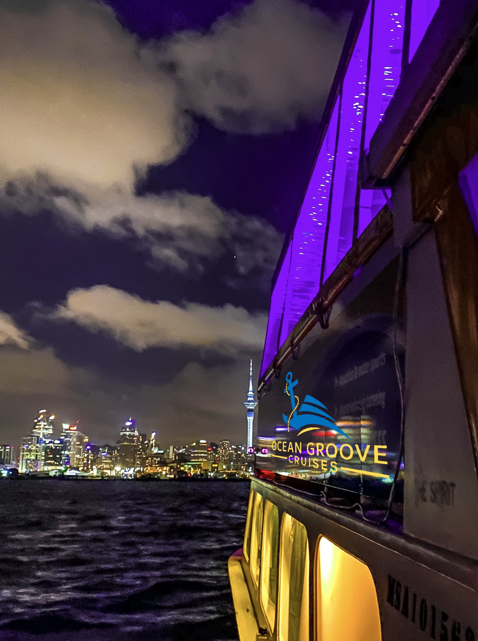 Ocean Groove Cruises' purple-lit party boat cruises Auckland Harbour against the sparkling city skyline.