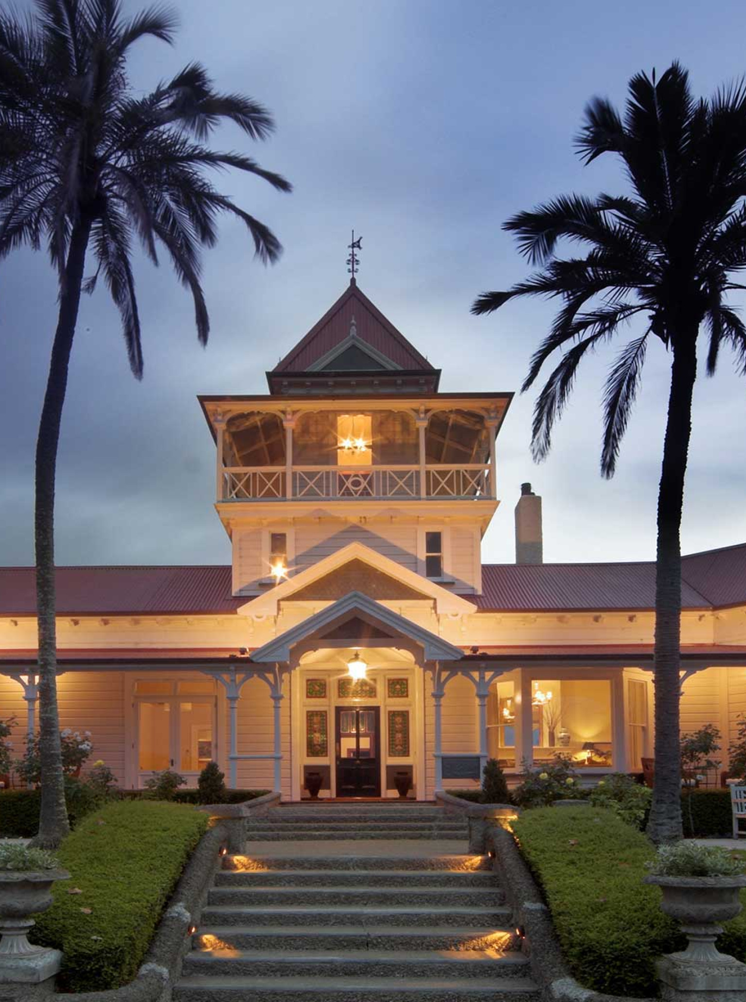 The illuminated entrance of Greenhill Lodge in Hawke's Bay, a historic Victorian-style homestead with a grand tower at dusk.