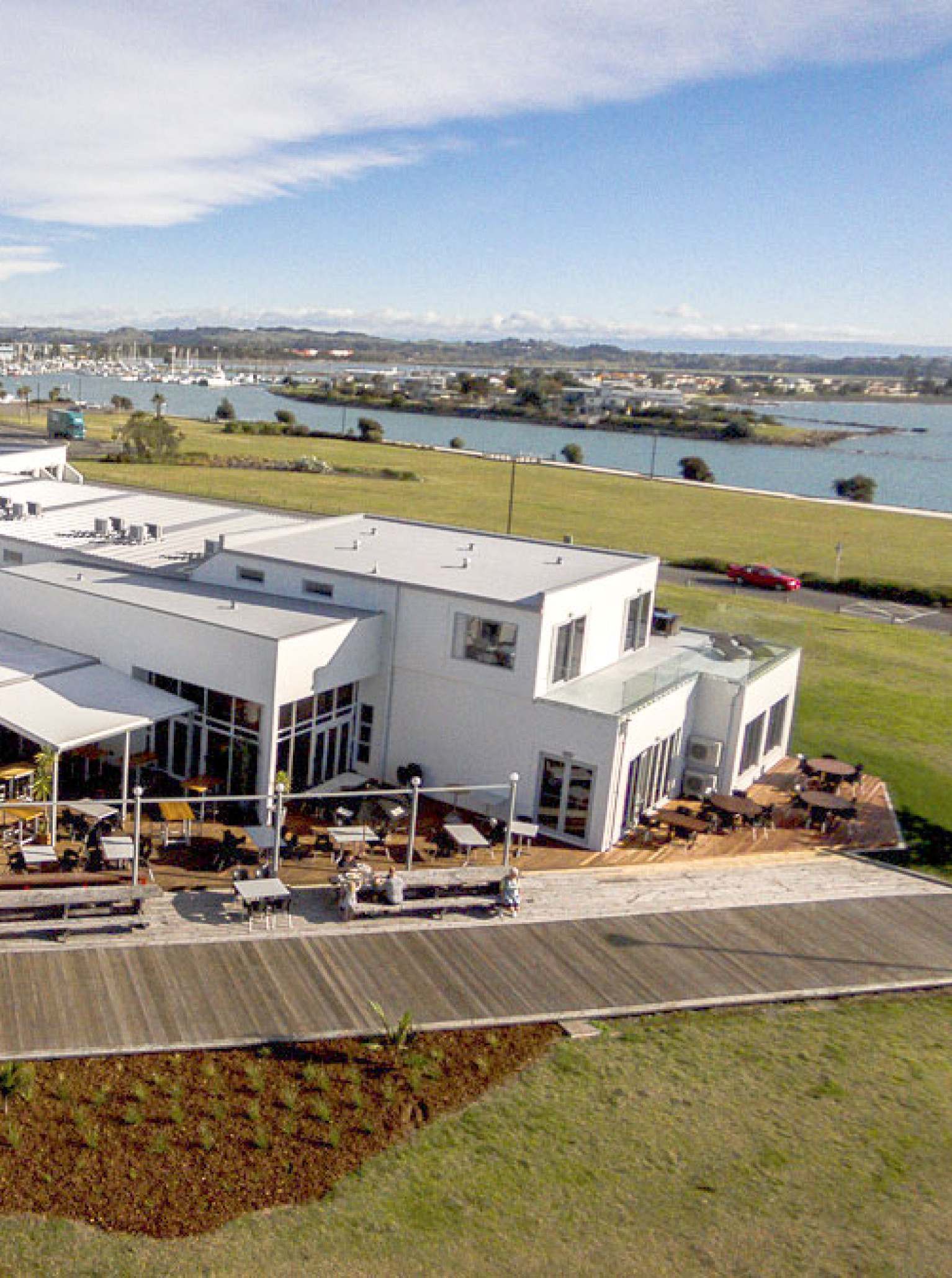 An aerial view of the modern East Pier Hotel in Hawke's Bay, featuring its waterfront brasserie and extensive outdoor decks.