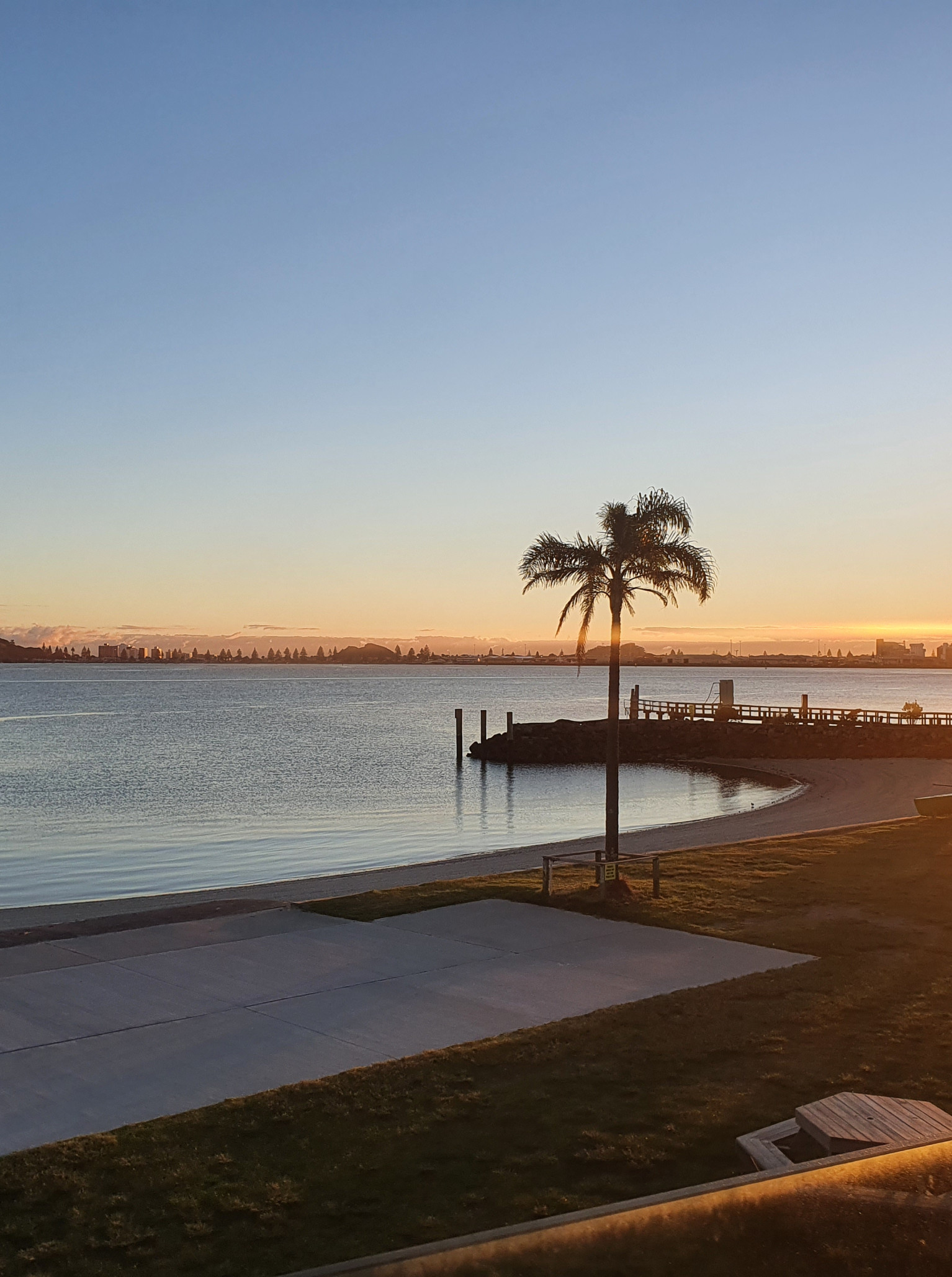 The Yacht Club in Tauranga offers panoramic waterfront views of the harbour and Mount Maunganui from its modern outdoor setting at sunrise.