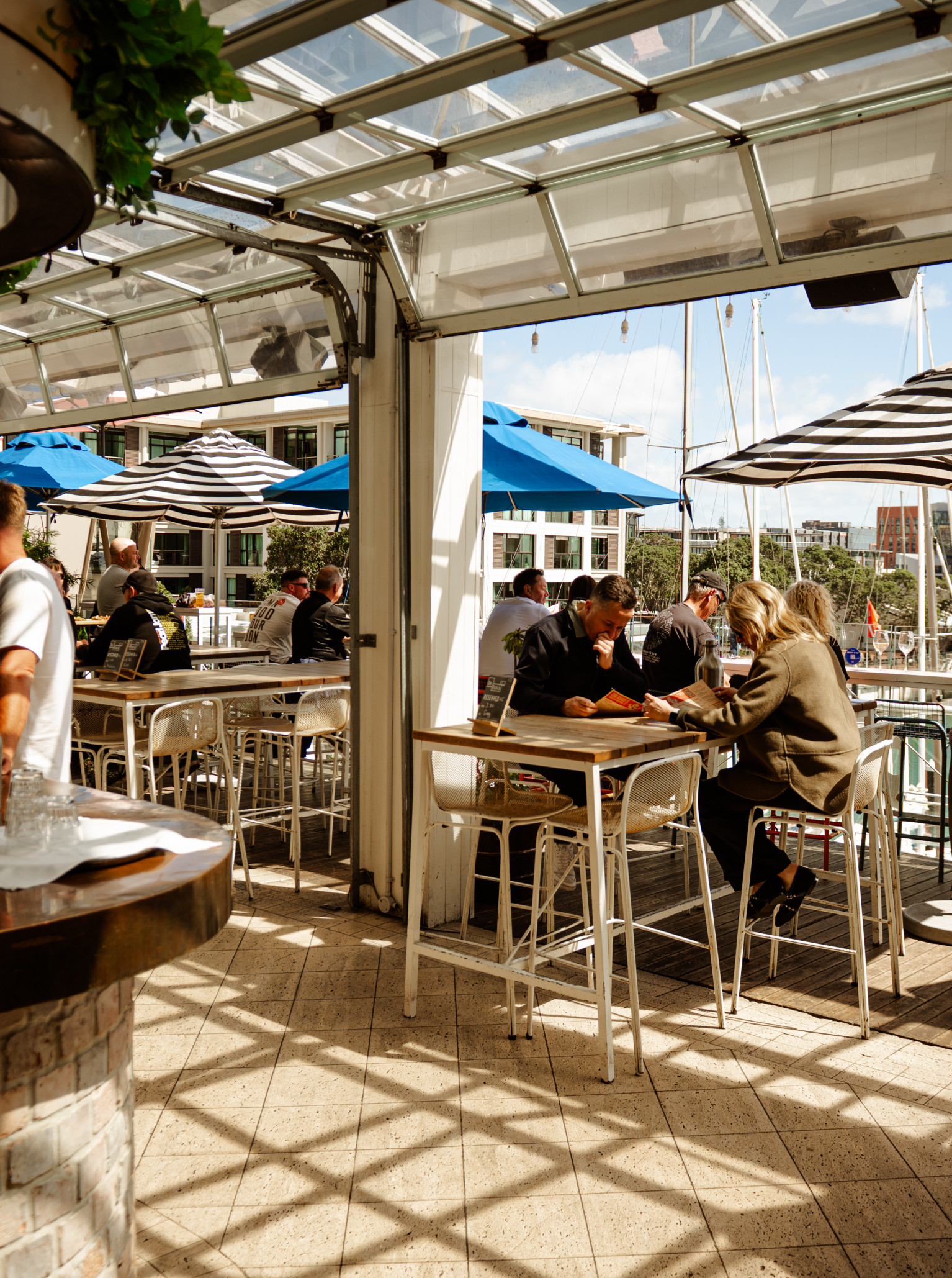 Patrons enjoy the vibrant, open-air rooftop bar at Dr Rudi's in Auckland, offering clear views of the Viaduct Harbour.