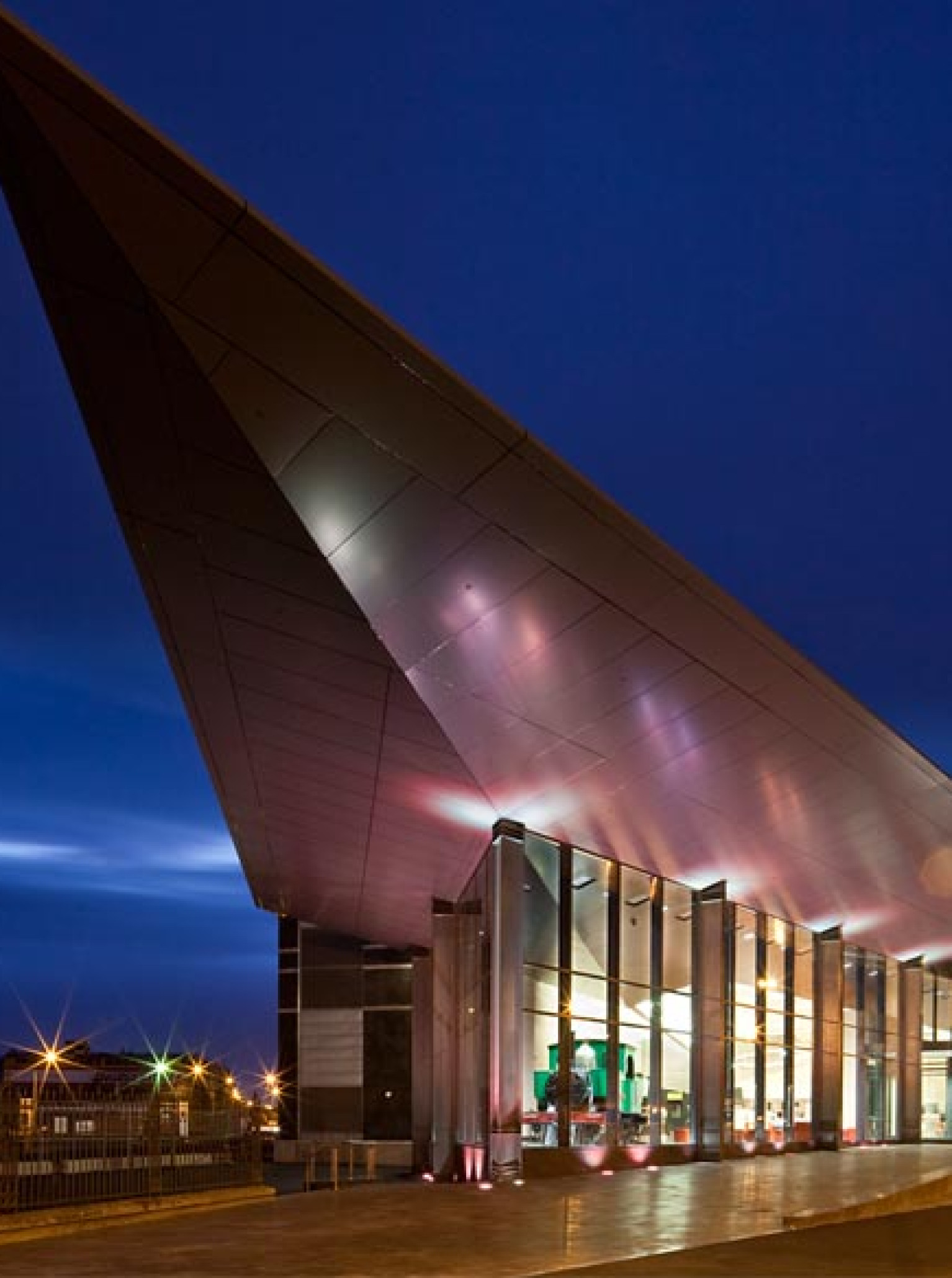 The modern, arrowhead-roofed entrance of the Toitu Otago Settlers Museum in Dunedin glows at night.