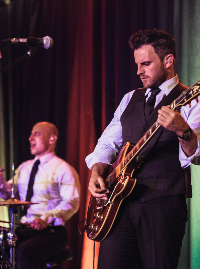 Auckland's Blue Steel band delivers a professional live music performance featuring a focused guitarist and energetic drummer on stage.