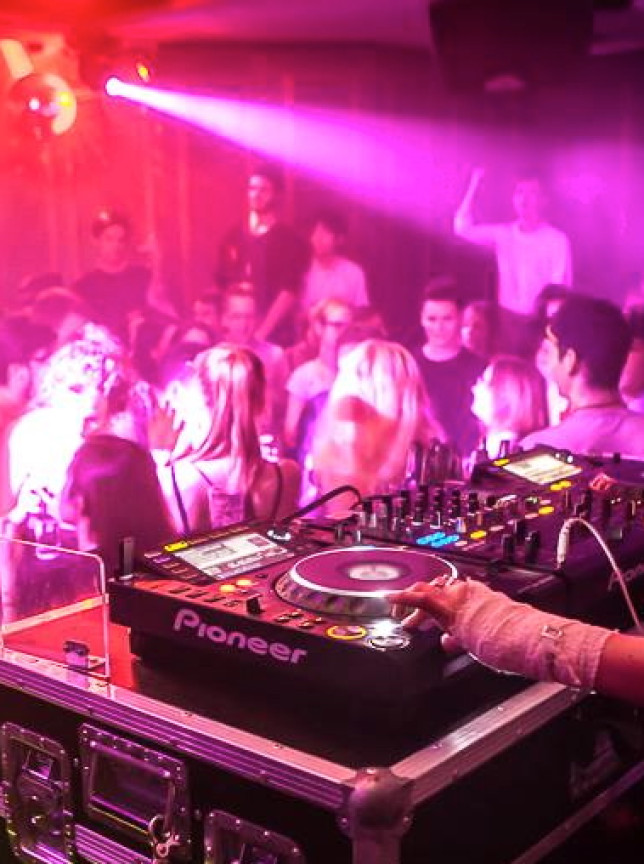 DJ Gabriella G plays to a lively dancing crowd in an energetic Auckland club bathed in red and purple lights.