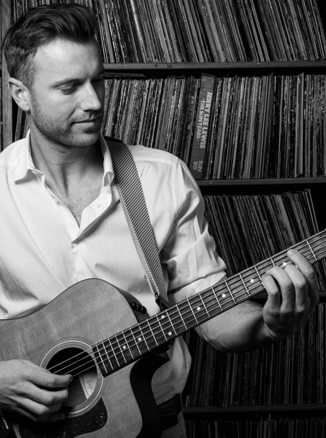 Auckland-based acoustic artist Daniel John plays his guitar, creating a relaxed ambiance amidst a collection of records.