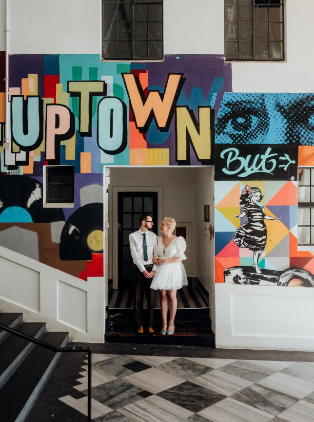 A couple poses in a vibrant urban art setting with a large mural, photographed by Chris Turner Photo & Video in Auckland.