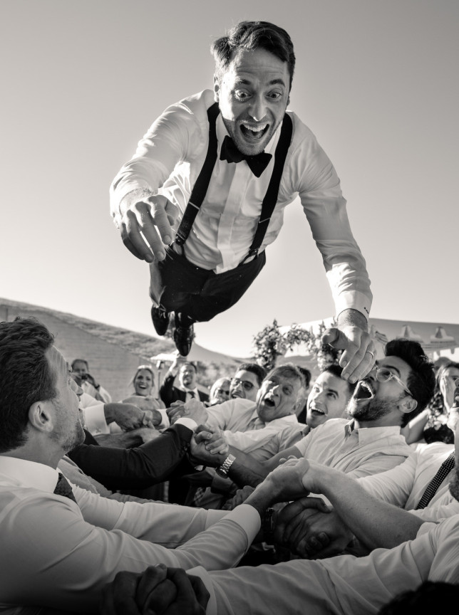A candid moment captured by Auckland's Zahn, showing a groom joyfully tossed in the air during an outdoor wedding celebration.