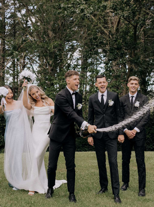 Rebecca Bradley Photography captures a joyful outdoor wedding celebration in Auckland, with the wedding party popping champagne.
