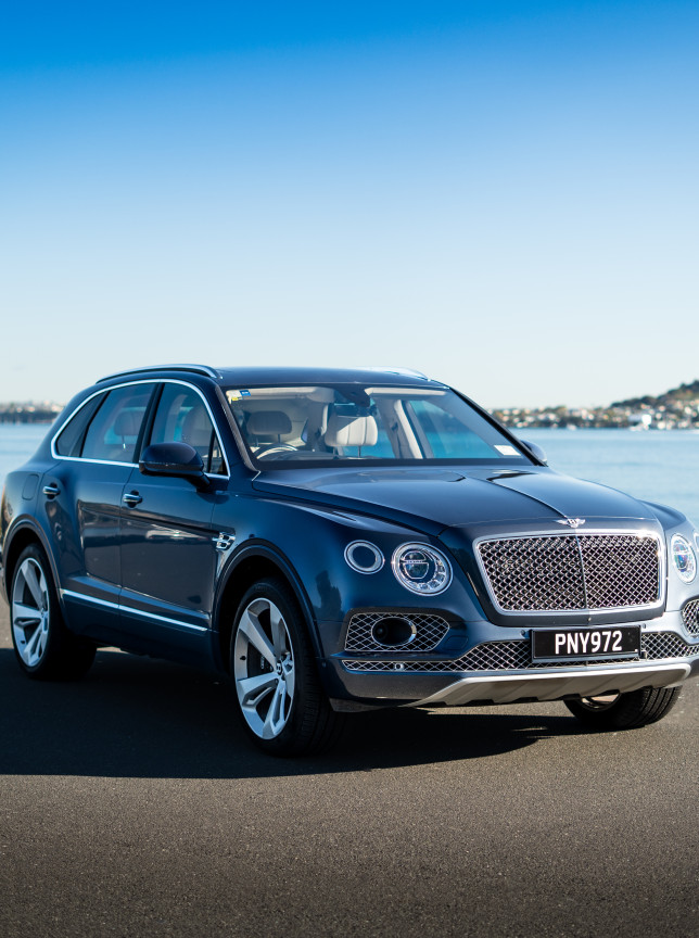 A luxury Bentley Bentayga SUV, offered by MotorShare Auckland, parked elegantly by the scenic waterfront.