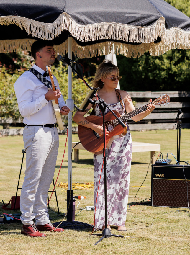 Amber Carly Williams provides live outdoor music at a Christchurch event, performing with another musician under a chic umbrella.