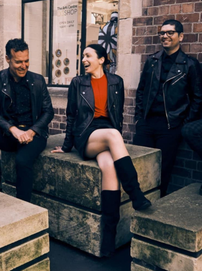 A group of people casually posed outdoors at The Arts Centre, Christchurch, a venue with historic stone and brick architecture.