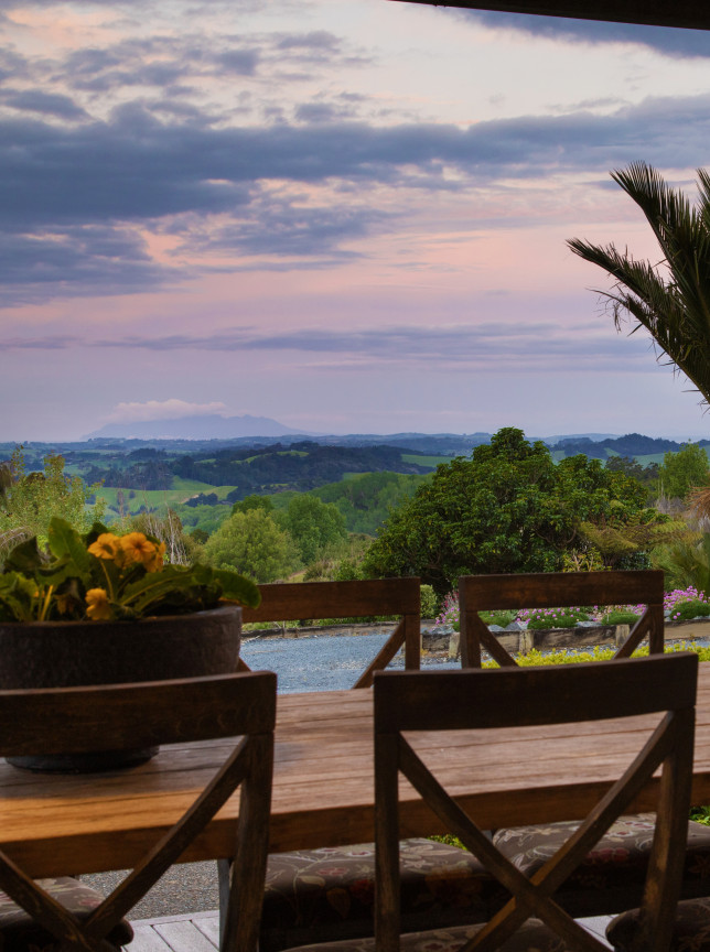 A contemporary outdoor dining patio at Woodhouse Mountain Lodge, Auckland, offers panoramic mountain and Hauraki Gulf views.