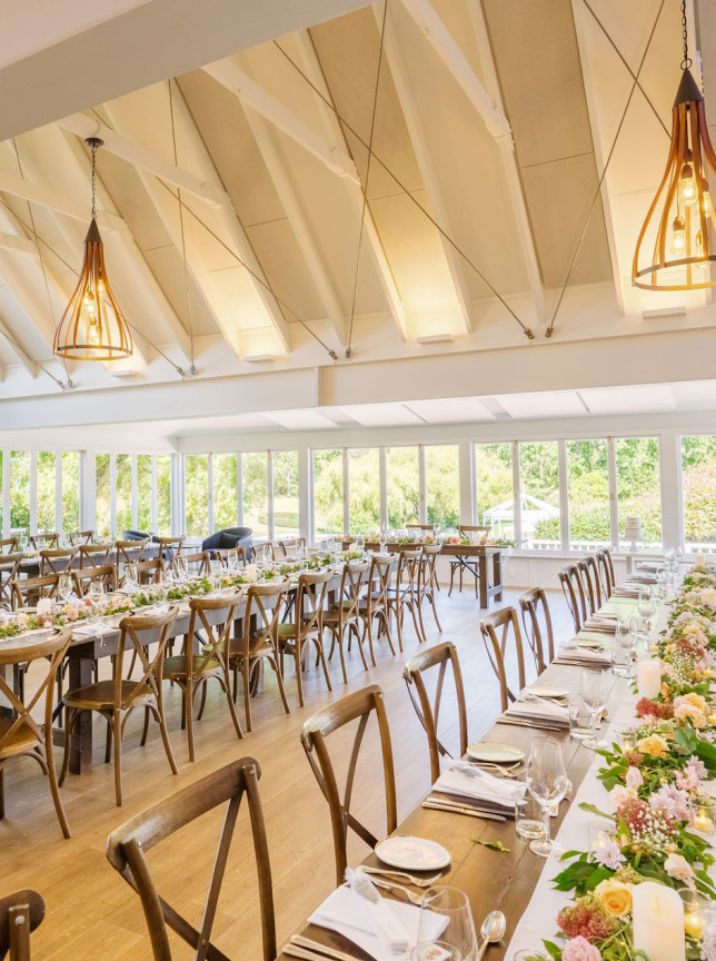 A bright, modern dining room at Abel Estate, Auckland, features renovated gabled ceilings and large windows overlooking lush grounds.