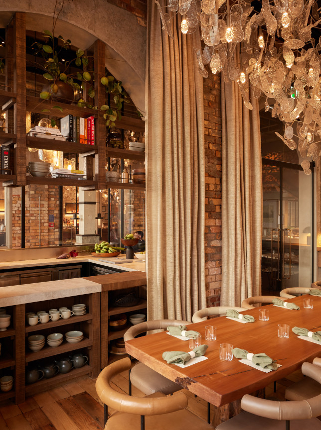 A sophisticated private dining room, Kingi Private, at The Hotel Britomart in Auckland, features a raw-edge timber table and a shimmering fish-scale chandelier.