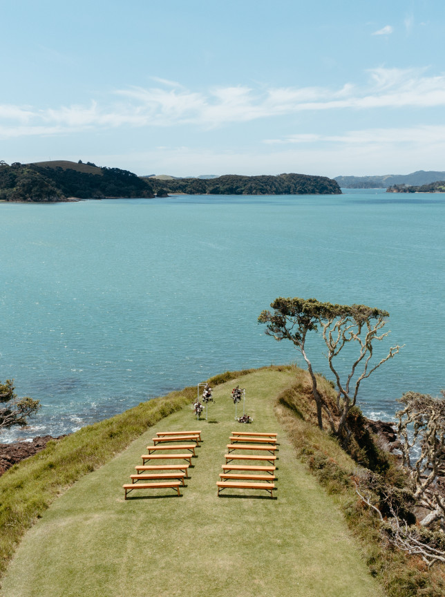 An outdoor wedding ceremony setup with wooden benches on The Point at Baylys' Farm, a stunning coastal venue in the Bay of Islands.