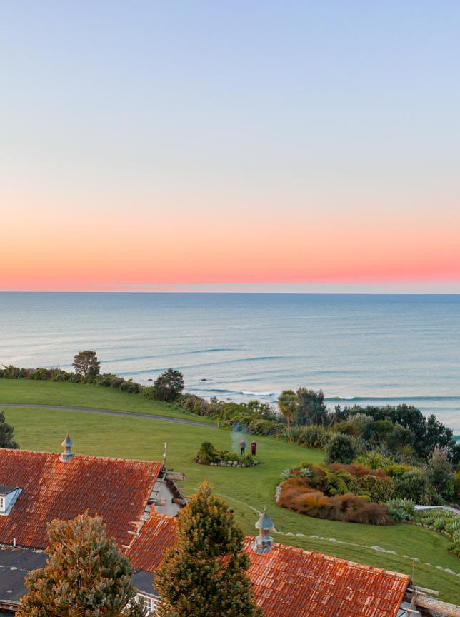 An aerial view of the European-styled Ahu Ahu Beach Villas in New Plymouth, featuring red-tiled roofs overlooking the ocean at sunset.