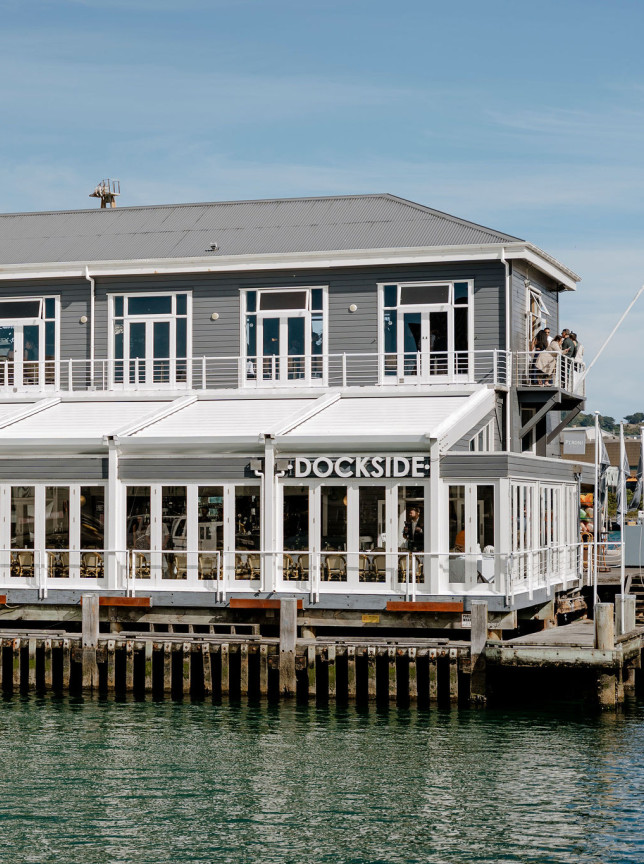 Wellington's historic Shed 3, home to Dockside Restaurant, is a grey, two-story building with white windows situated over the water.