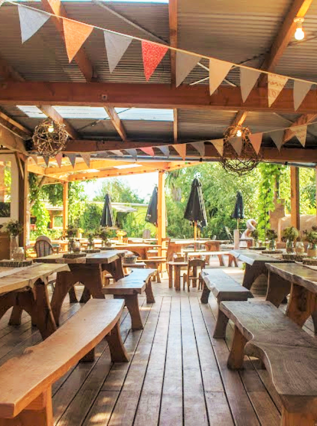 Toad Hall, a charming rustic outdoor dining area in Nelson-Tasman, features communal wooden tables with festive bunting.