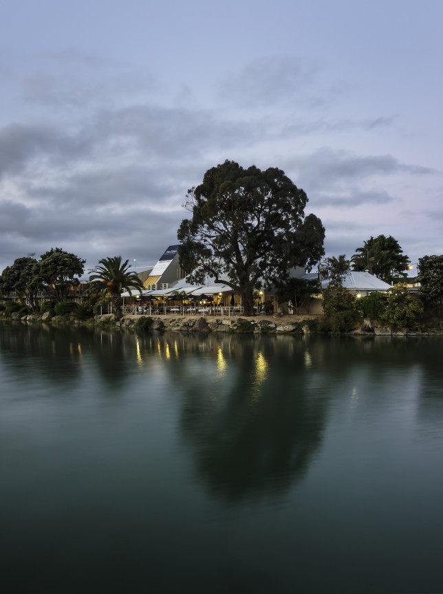 The stylish Tides Hotel in Nelson-Tasman features contemporary riverfront dining with illuminated outdoor areas at dusk.