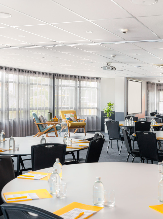 Contemporary, light-filled meeting room at WQ Hotel, Wellington, arranged with round tables and a lounge area.