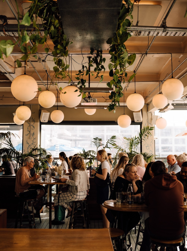 The vibrant, modern indoor-outdoor dining area of Saint Alice in Auckland, adorned with lush plants and globe lights.
