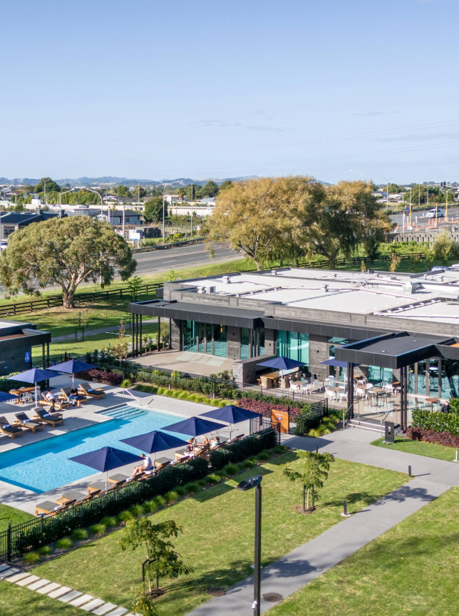 An aerial view of the DoubleTree by Hilton Auckland Karaka's modern outdoor pool and contemporary hotel buildings.