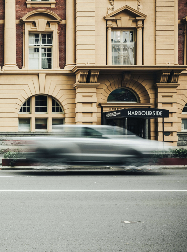 The elegant Edwardian Baroque exterior of Harbourside Ocean Bar Grill at Auckland's historic Ferry Building, with cars blurring past.
