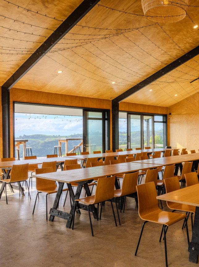 The Black Barn at Vanderosa Farms in Auckland features a natural wood event space with long dining tables, fairy lights, and stunning views.
