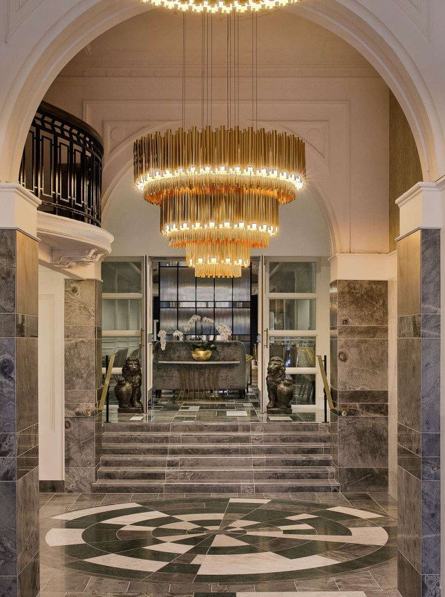 The opulent Art Deco grand lobby at Fable Auckland features arched ceilings, marbled details, and a tiered chandelier.