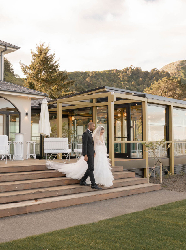 A newlywed couple strolls on the sleek, contemporary outdoor deck at The Hilltop, a modern wedding venue in Christchurch.