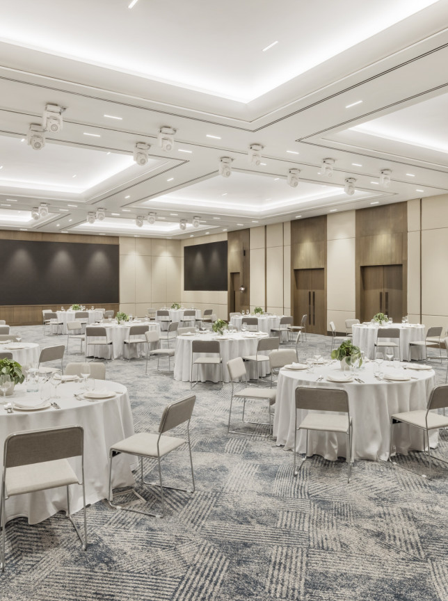 A modern, elegant banquet setup in the pillarless ballroom of JW Marriott Auckland, featuring neutral tones and warm wood accents.