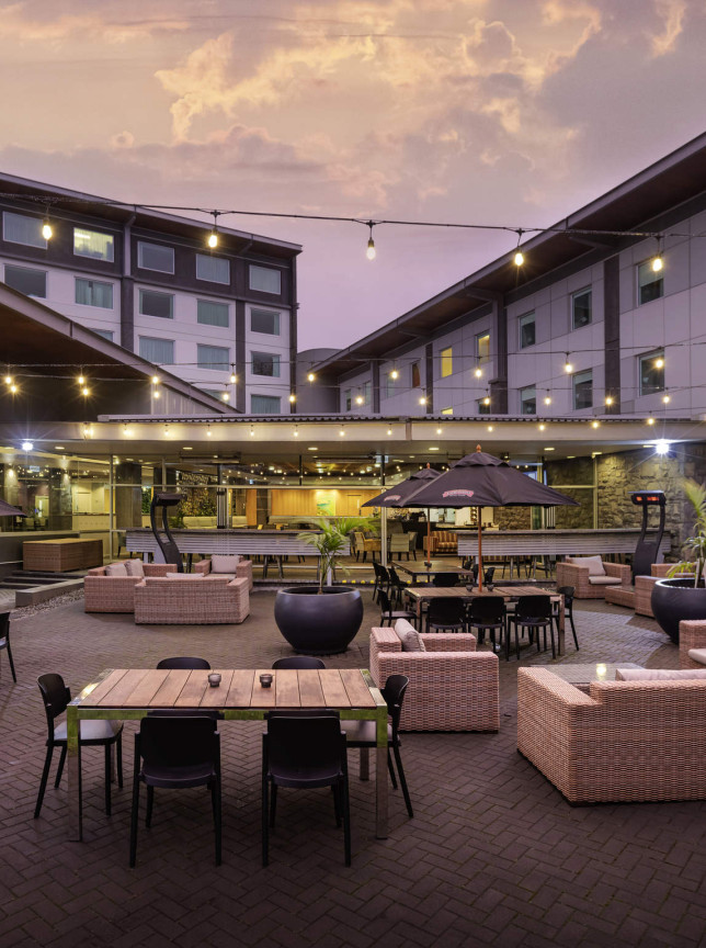A modern outdoor courtyard patio at Novotel Auckland Ellerslie, featuring comfortable seating and string lights at dusk.