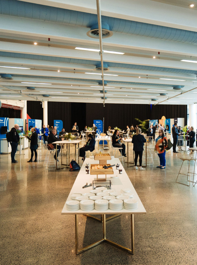 Attendees mingle in the Viaduct Events Centre, Auckland, a modern, industrial-chic event space with polished concrete floors and exposed ceilings.