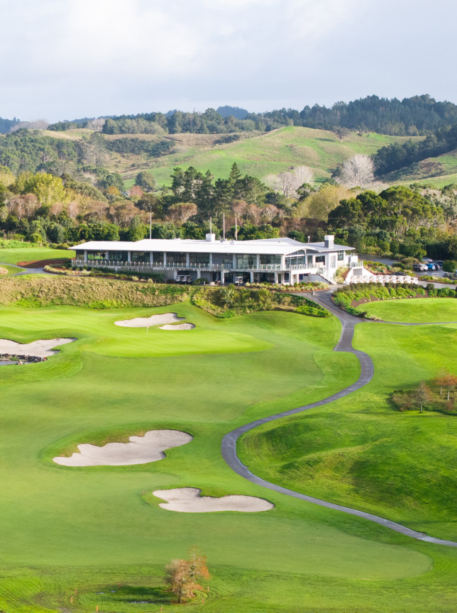 A modern, architecturally designed clubhouse at Wainui Golf Club, Auckland, overlooks lush green fairways and rolling hills.